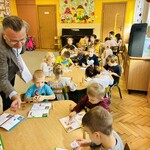 dzieci siedzą przy stolikach i kolorują kolorowanki