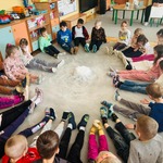 dzieci siedzą na dywanie w kręgu, między nimi unosi się pra